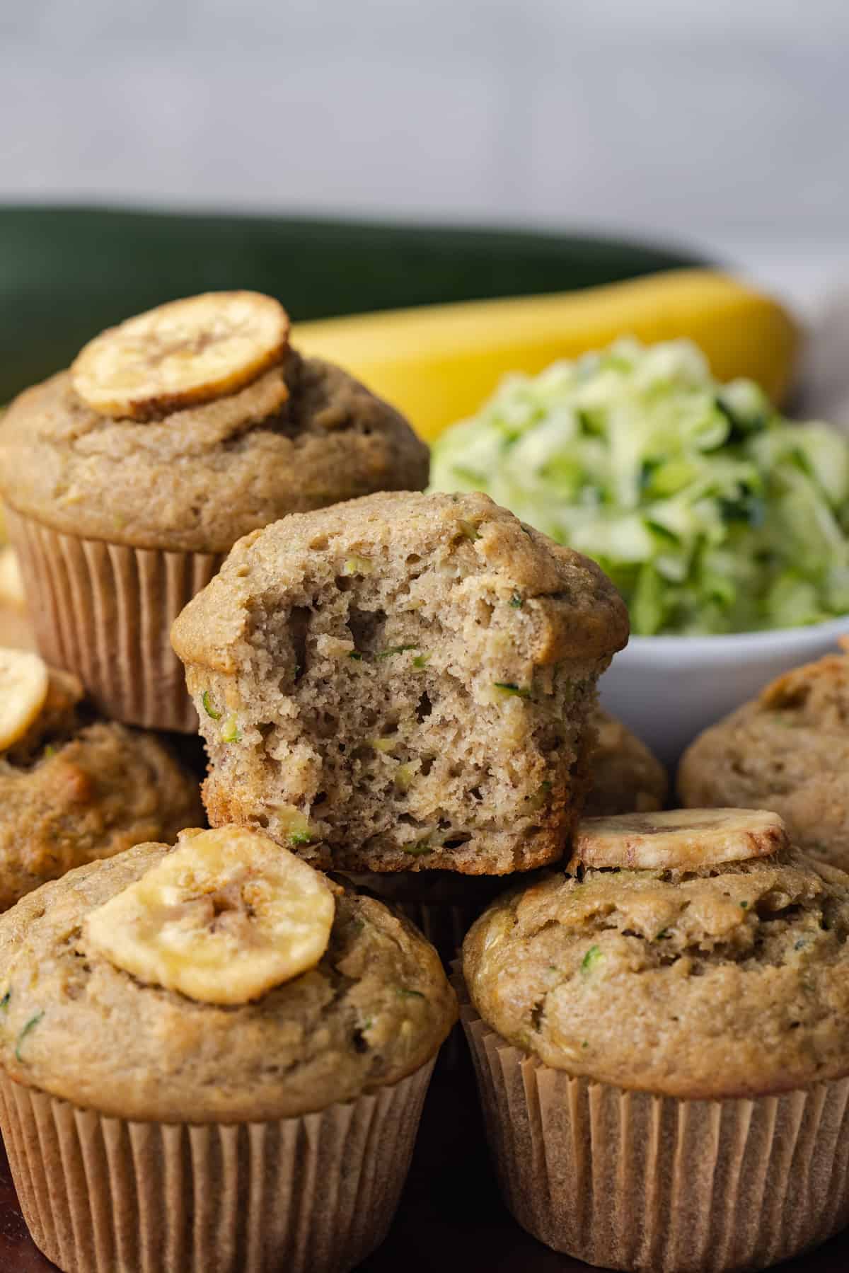 Zucchini banana muffins stacked with a bite taken out of the top one so the fluffy inside is visible.