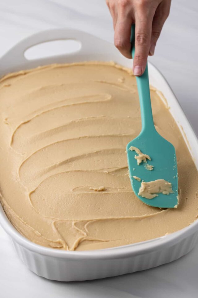 A blue spatula spreading brown sugar frosting on banana cake
