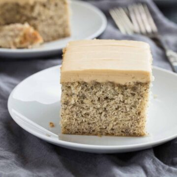 A slice of Easy Banana Cake recipe topped with luscious brown sugar frosting on a white plate.