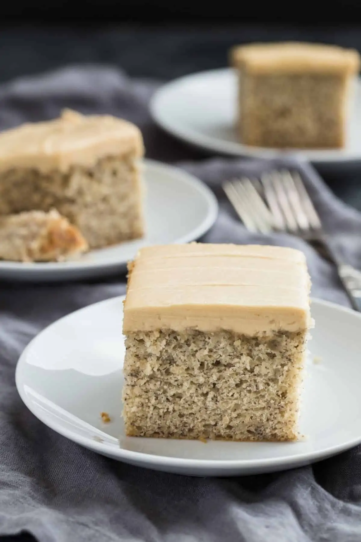 A slice of Easy Banana Cake recipe topped with luscious brown sugar frosting on a white plate.