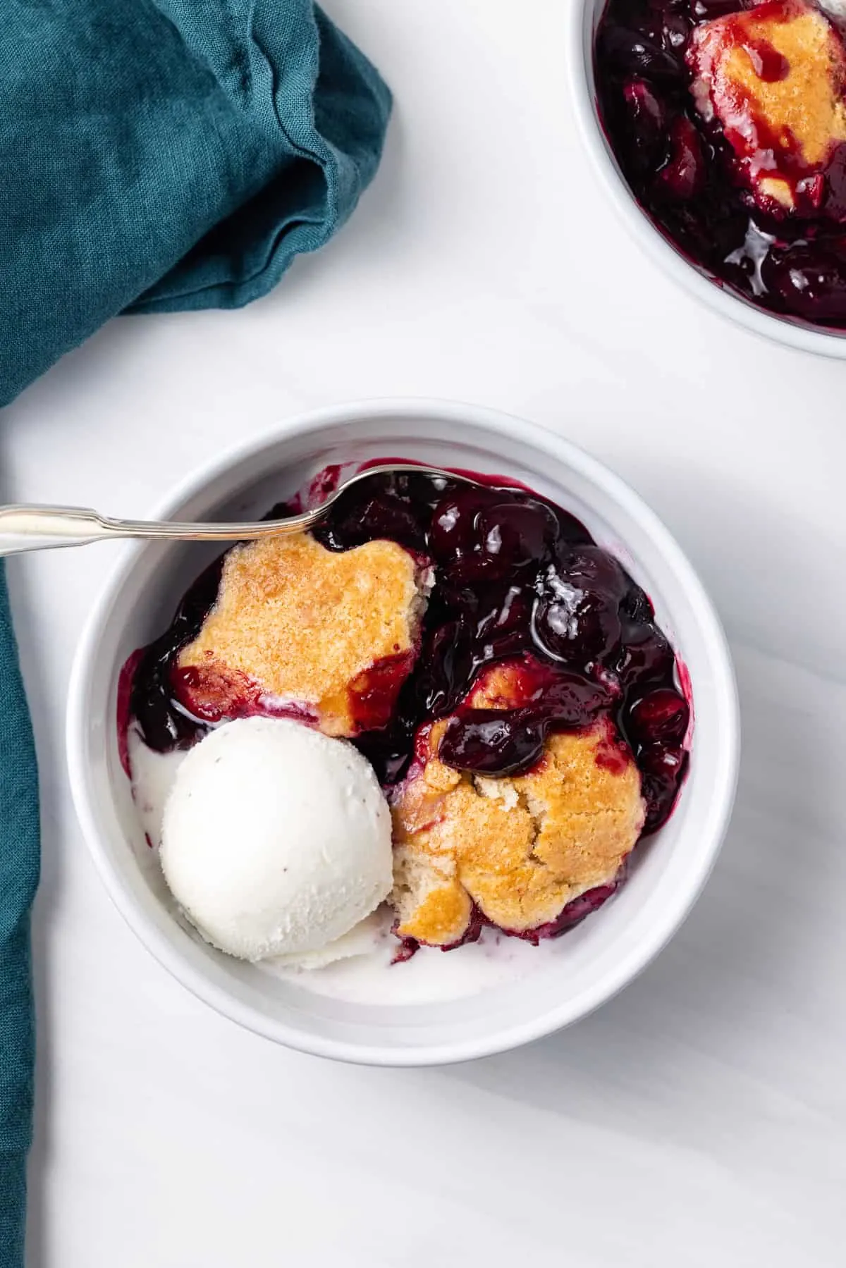 A white bowl of cherry cobbler with a scoop of ice cream