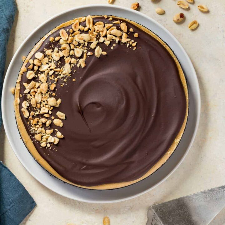 Overhead view of chocolate peanut butter cheesecake on a white plate with a blue napkin beside it.