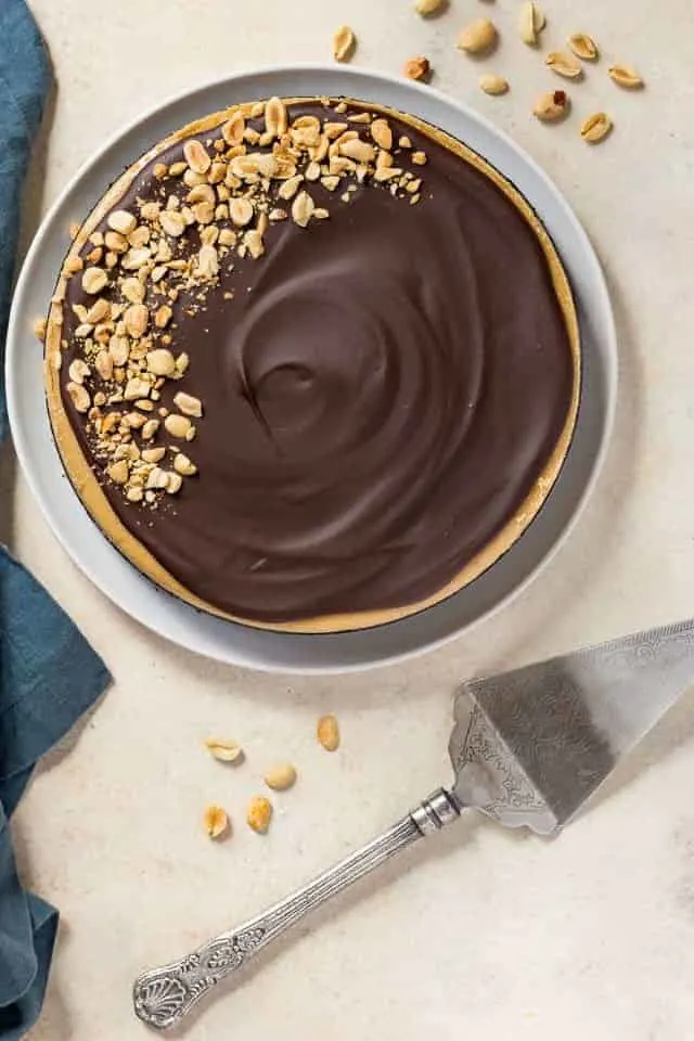 Overhead view of chocolate peanut butter cheesecake on a white plate with a blue napkin beside it.