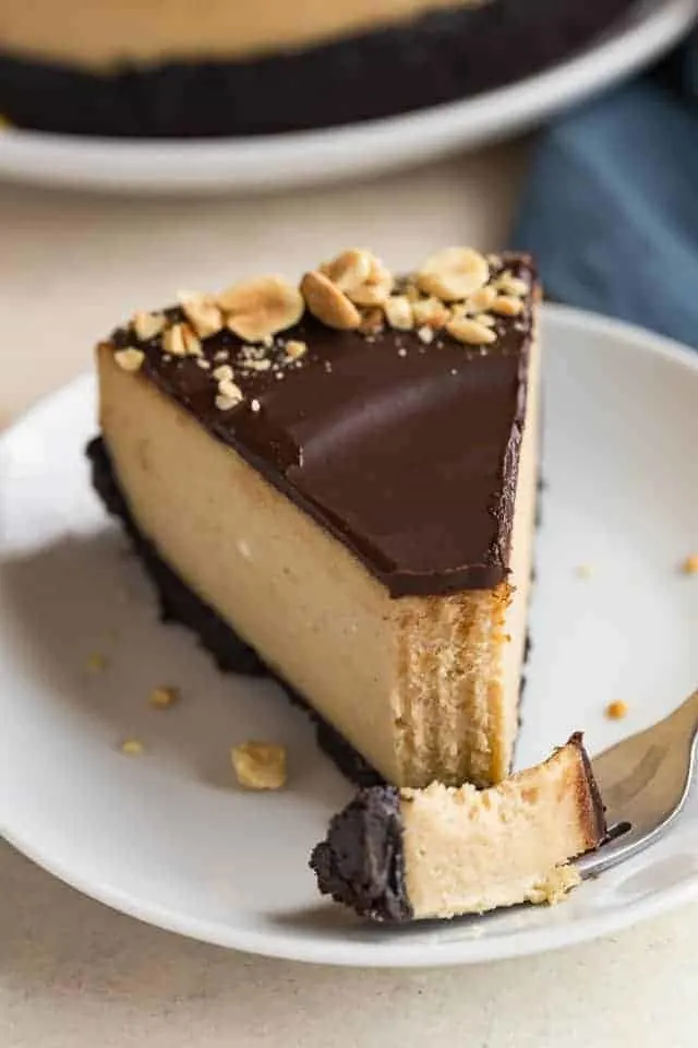 A slice of chocolate peanut butter cheesecake on a white plate with a fork taking a bite out.