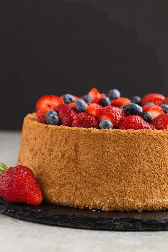 side view of an angel food cake topped with fresh strawberries and blueberries