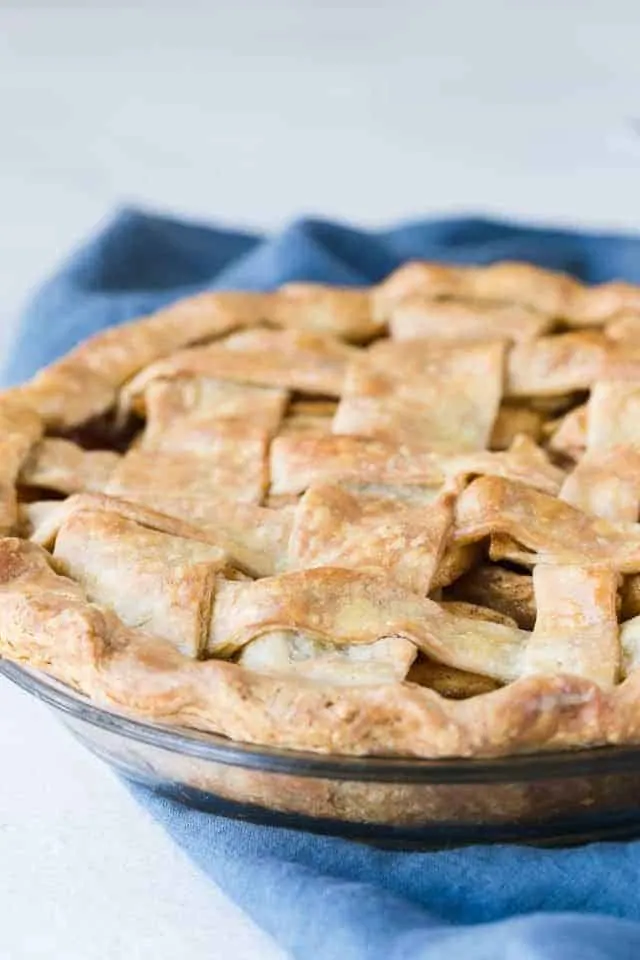 A lattice top apple pie in a glass pie dish sitting on a blue napkin.