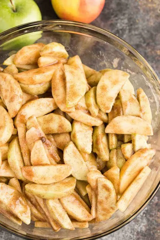 A glass bowl filled with apples coated in cinnamon and brown sugar.