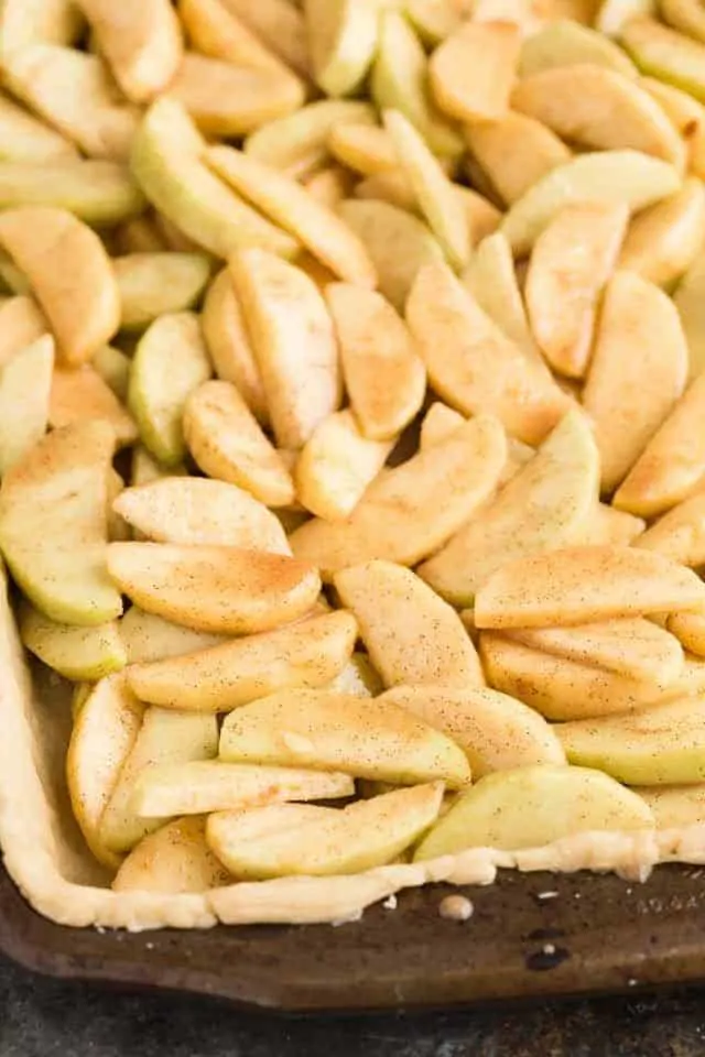 A large unbaked pie crust filled with apples coated in cinnamon and brown sugar.