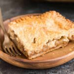 A square slice of apple slab pie on a wooden plate with a fork next to it.