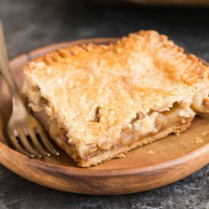A square slice of apple slab pie on a wooden plate with a fork next to it.