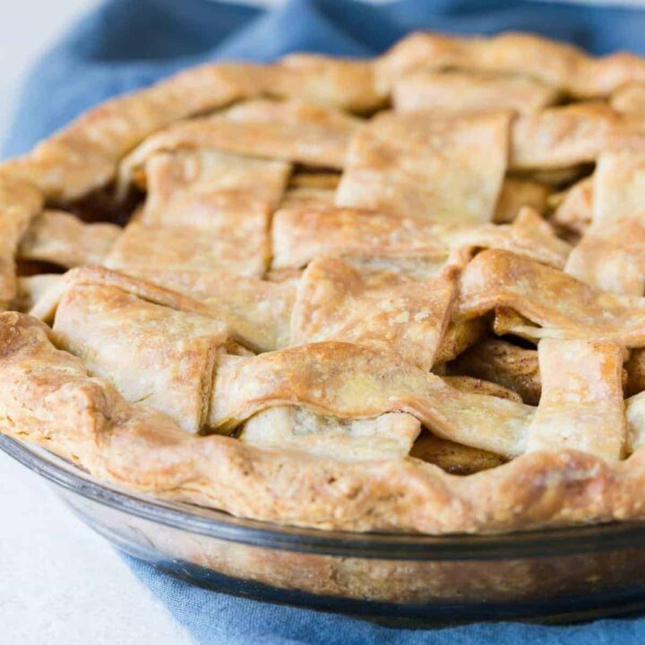 A lattice top apple pie in a glass pie dish sitting on a blue napkin.