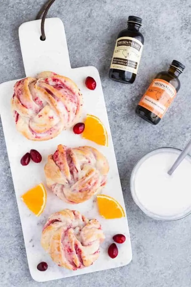 Cranberry orange sweet rolls on a marble cutting board decorated with fresh cranberries and orange slices.