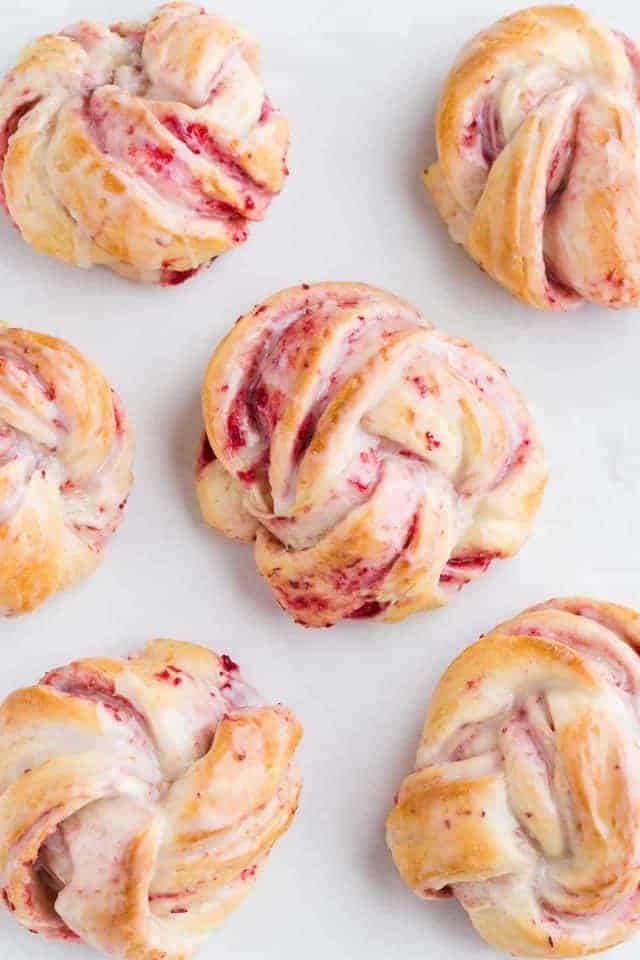 Six cranberry orange sweet rolls on a baking sheet lined with parchment paper.