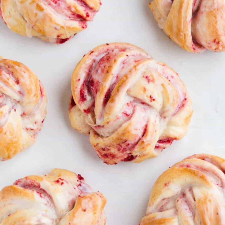 Six cranberry orange sweet rolls on a baking sheet lined with parchment paper.