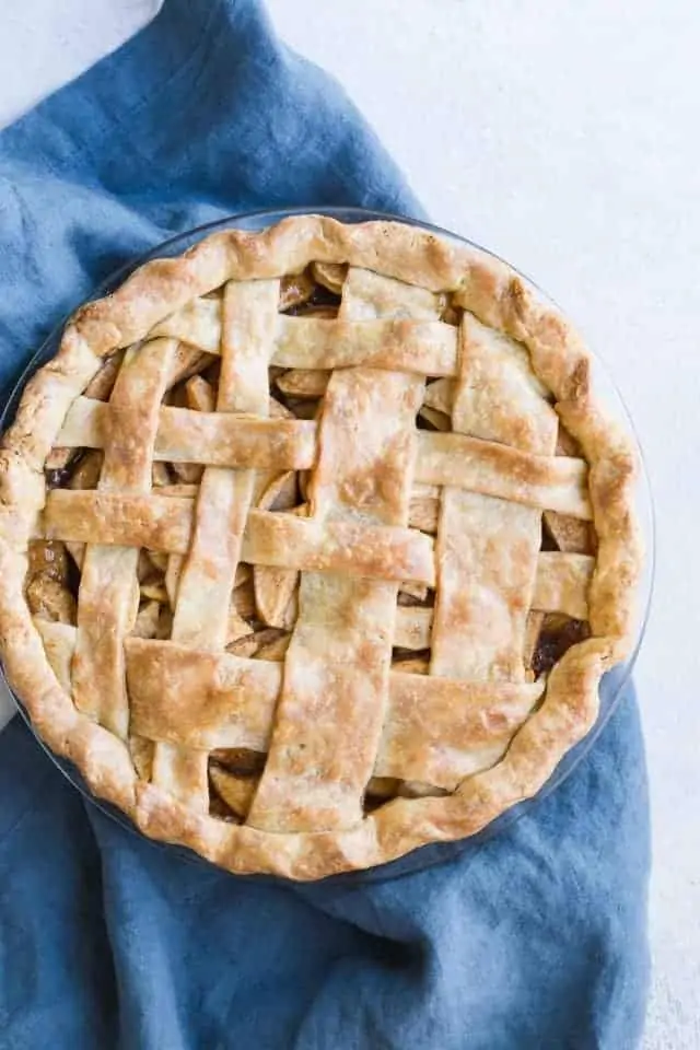 Gorgeous overhead view of a baked apple pie with brown butter crust sitting on a dark blue napkin.