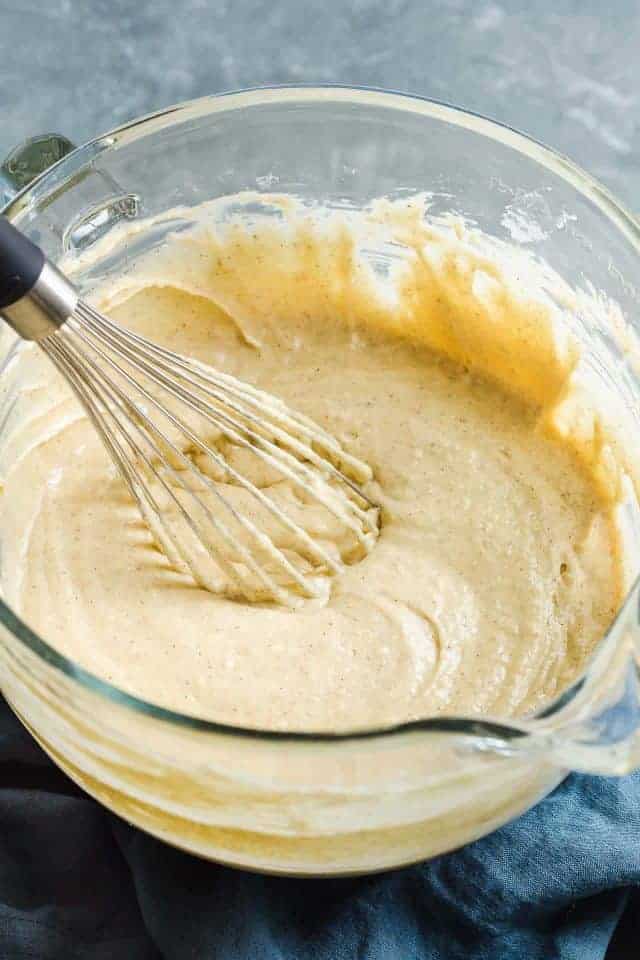Eggnog cake batter in a glass mixing bowl with a wire whisk.