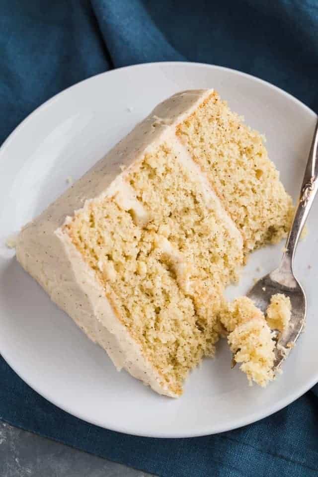 Slice of eggnog cake on a white plate with a fork taking a bite out.