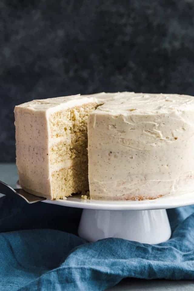 Eggnog cake on a white cake stand with a slice being taken out.