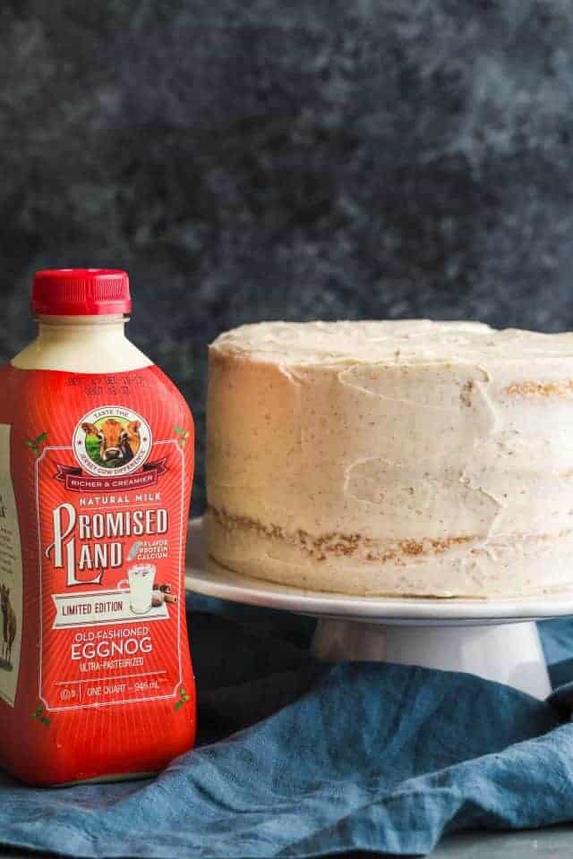 Eggnog cake on a white cake stand with a bottle of Promised Land Dairy Old Fashioned Eggnog next to it.