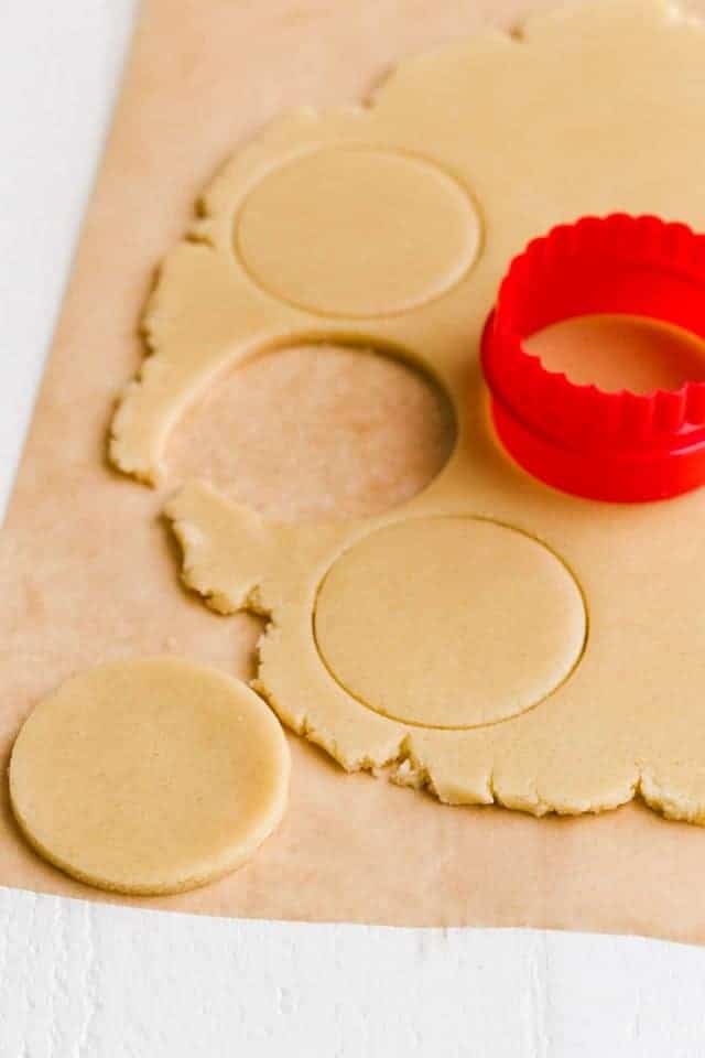 Cookie dough being cut with round red cookie cutter.
