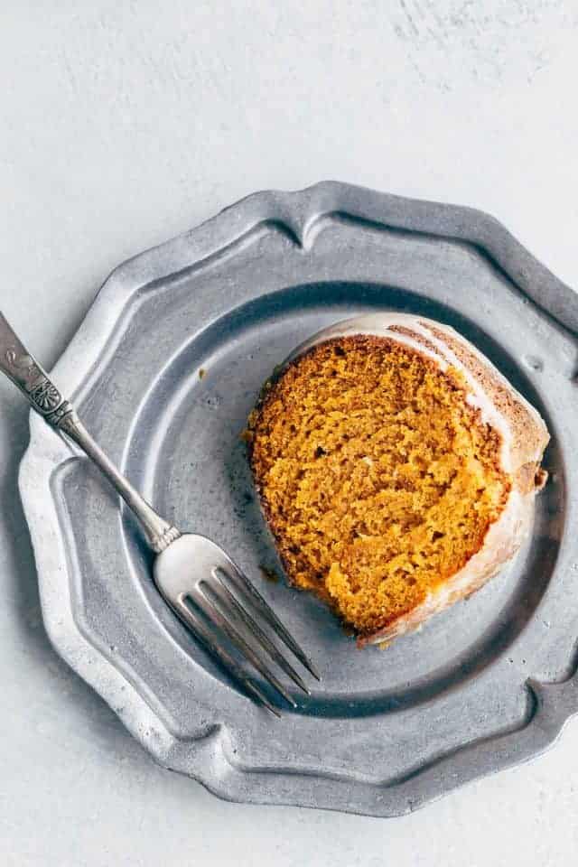 An overhead shot of a slice of pumpkin bundt cake sitting on a pewter plate with a fork next to it.