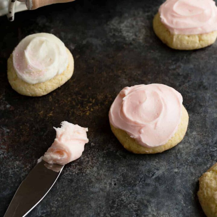 Frosted sour cream cookies next to a spreading knife with frosting on the tip.
