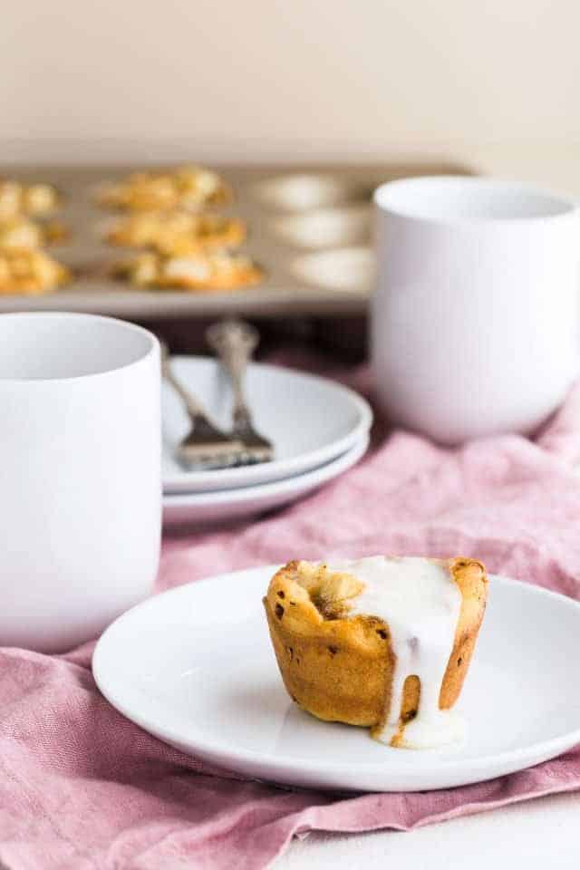 Apple Pie Cinnamon Roll Cup on a white plate with glaze dripping down the side.