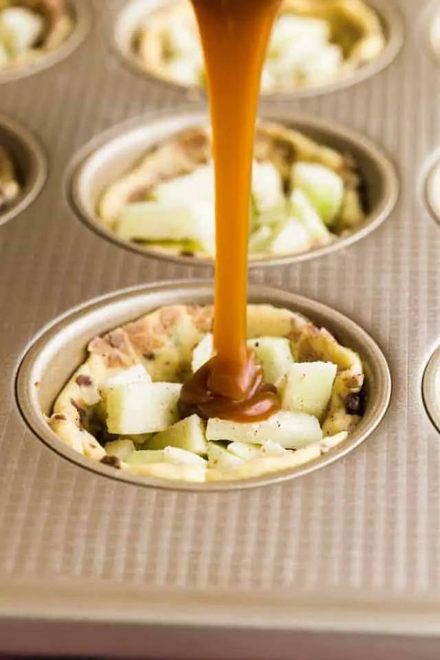 Apple pie cinnamon roll cups in a muffin tin being topped with caramel sauce.