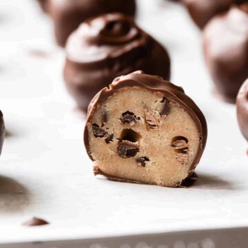 cookie dough truffles on a baking sheet with one cut in half so the inside is visible.