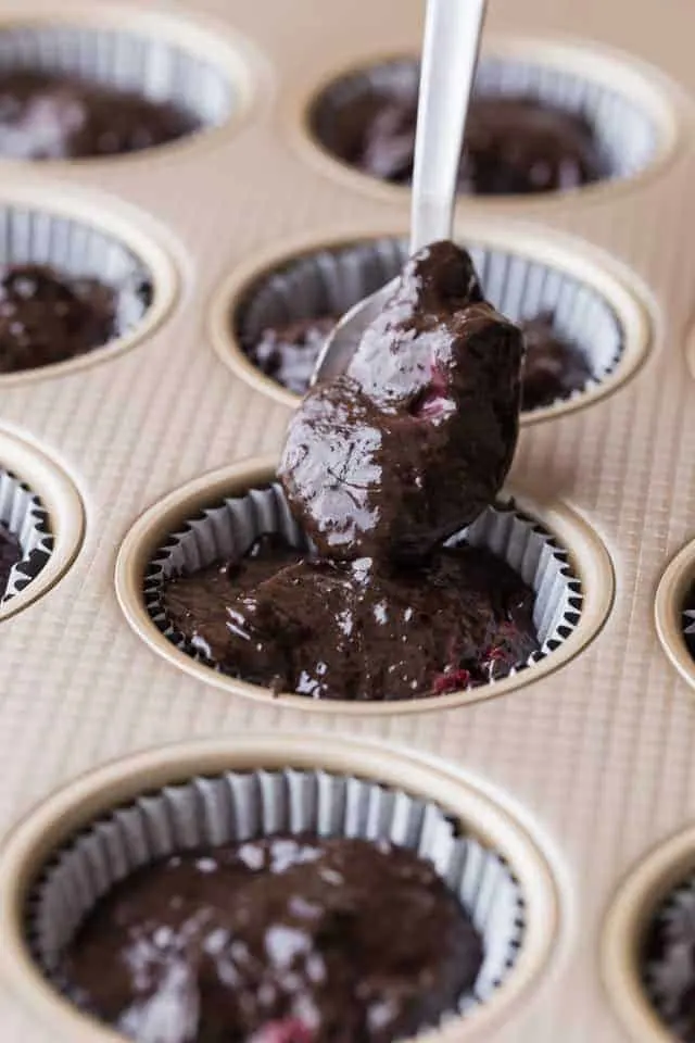 Chocolate muffin batter getting spooned into a gold muffin pan.