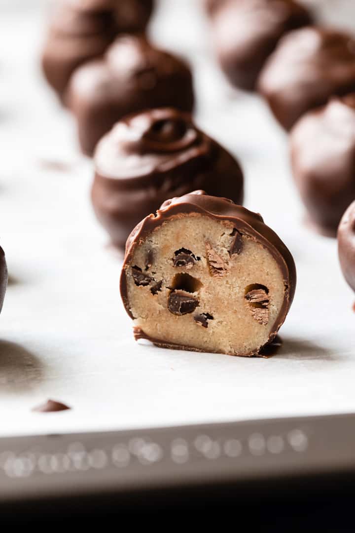 cookie dough truffles on a baking sheet with one cut in half so the inside is visible.