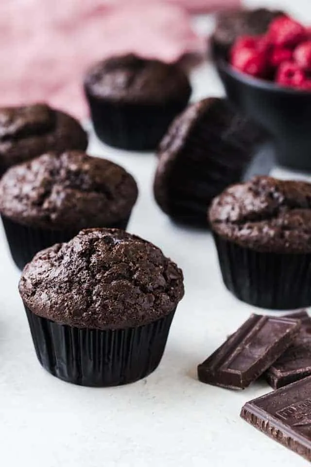 Double chocolate raspberry muffins on a white tabletop with bits of chocolate next to them.