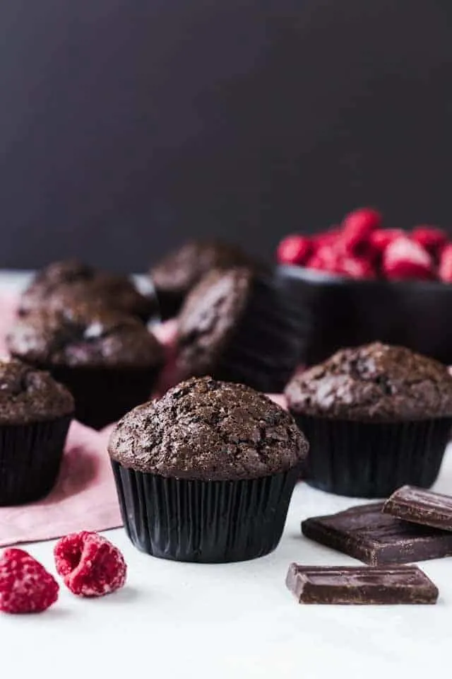 Double chocolate muffins with raspberries on a white tabletop with a pink napkin.