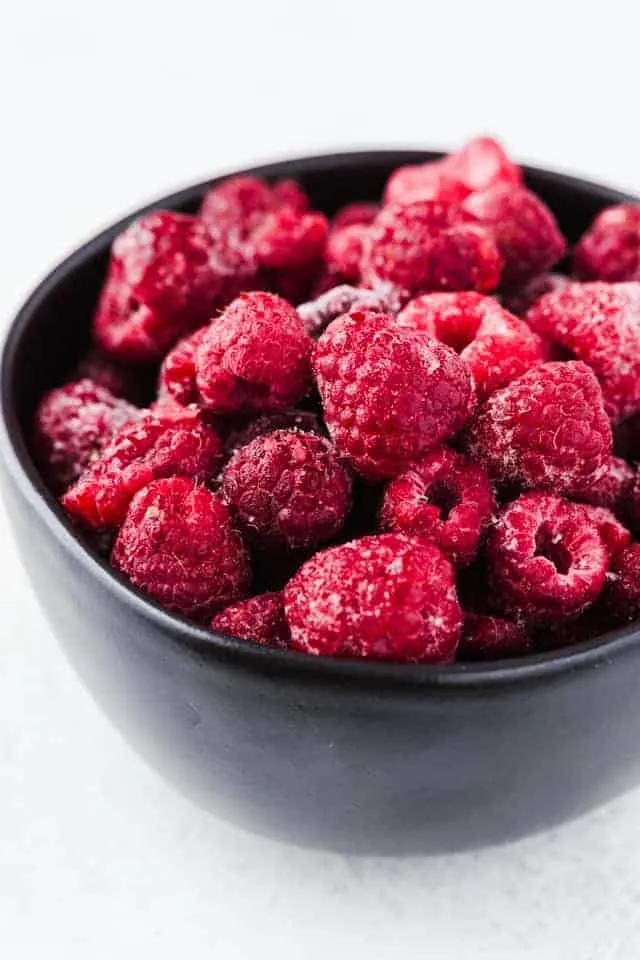 Raspberries in a black bowl on a white background.