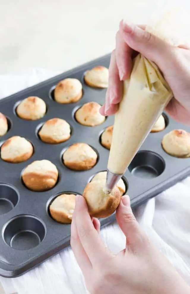 Baked bunuelos being filled with anise filling.