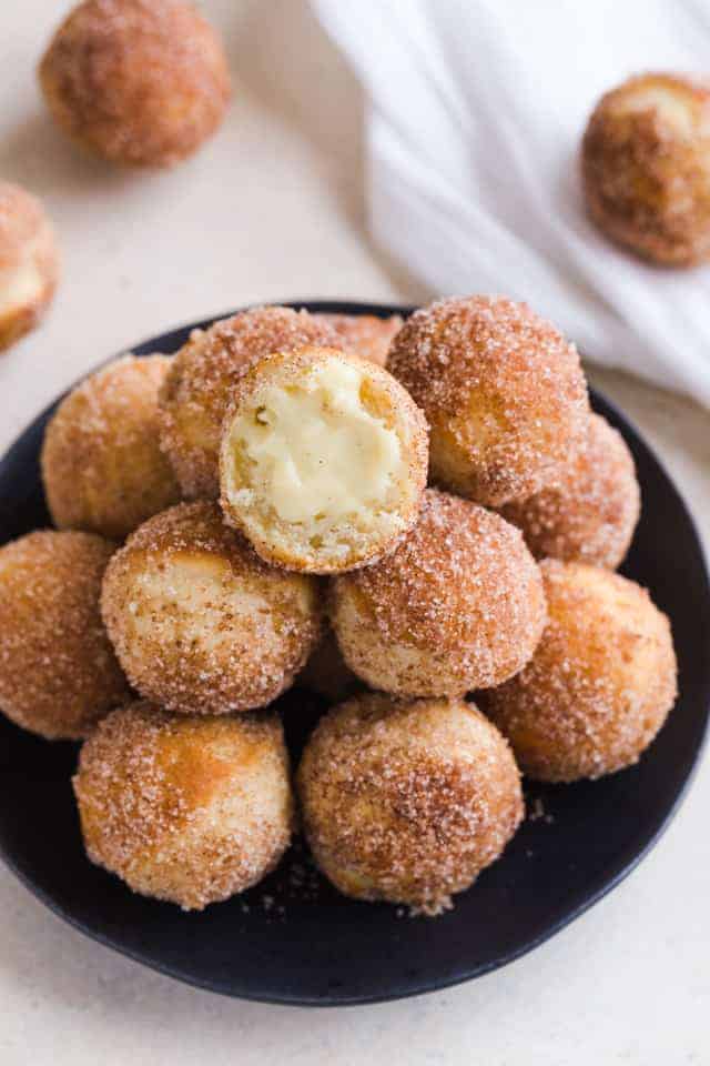 Close up of baked bunuelos with anise filling on a black plate.