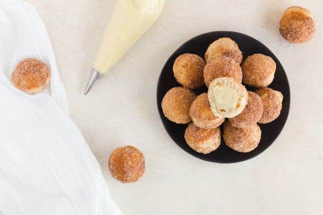 Overhead view of baked bunuelos with anise filling on a black plate.