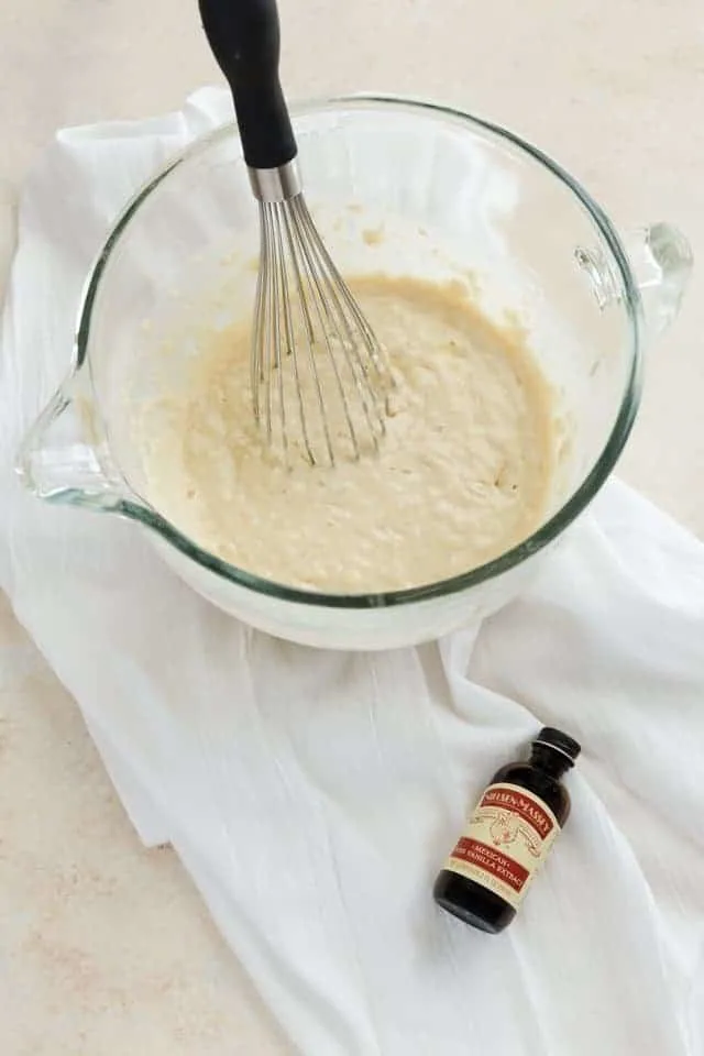 Bunuelos batter in a clear bowl with a whisk.