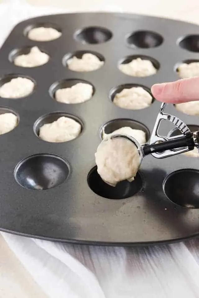 Bunuelos batter being spooned into a donut hole pan.