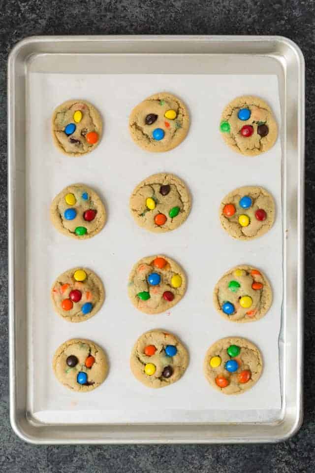 M&M cookies on an aluminum baking sheet lined with parchment paper.