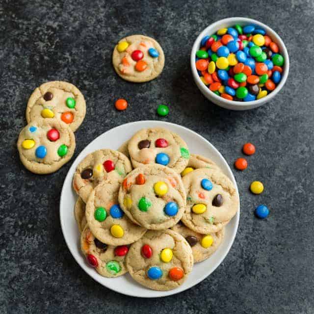 M&M cookies on a white round plate next to a bowl of m&m's.