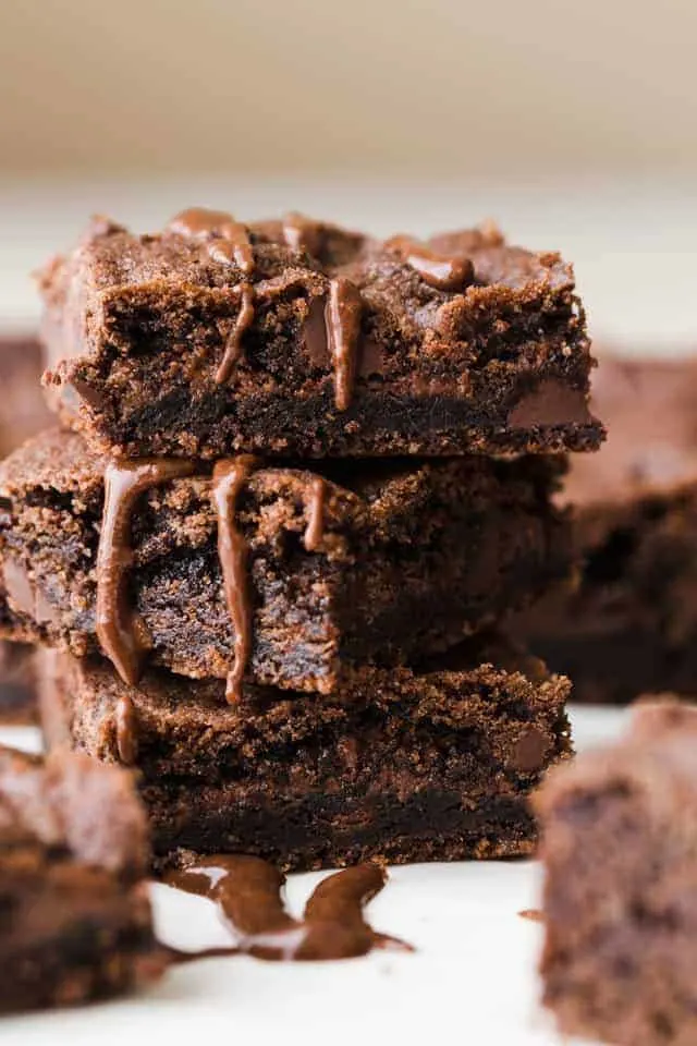 Three chocolate nutella cookie bars stacked on white parchment paper and drizzled with nutella.