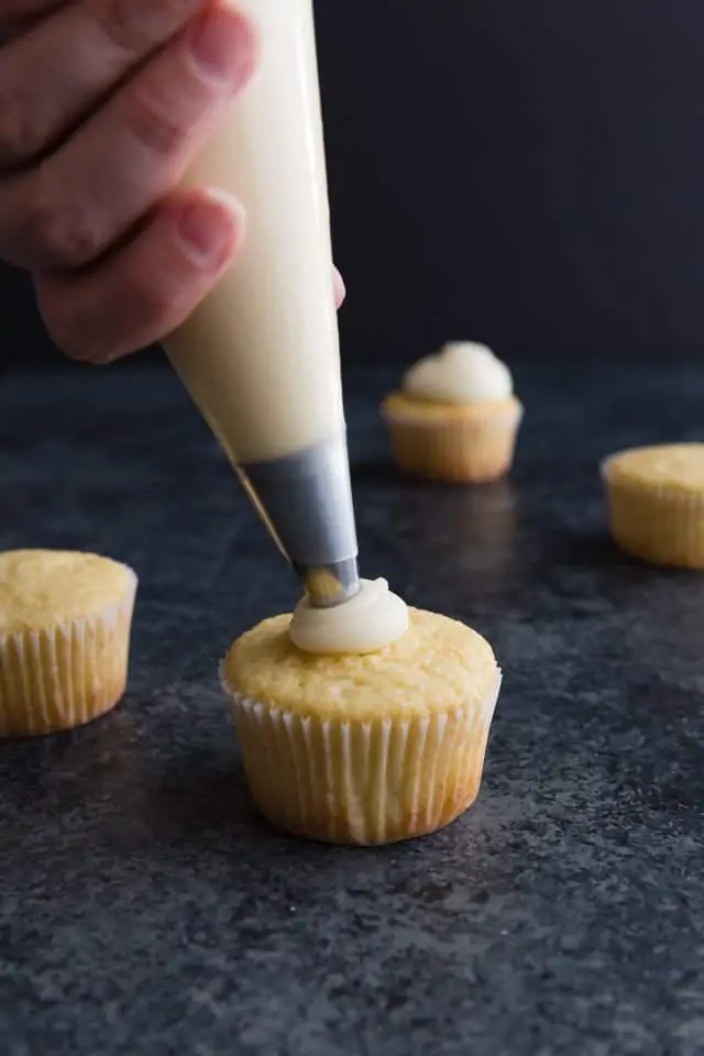 Lemon cream cheese frosting being piped on top of cupcakes.