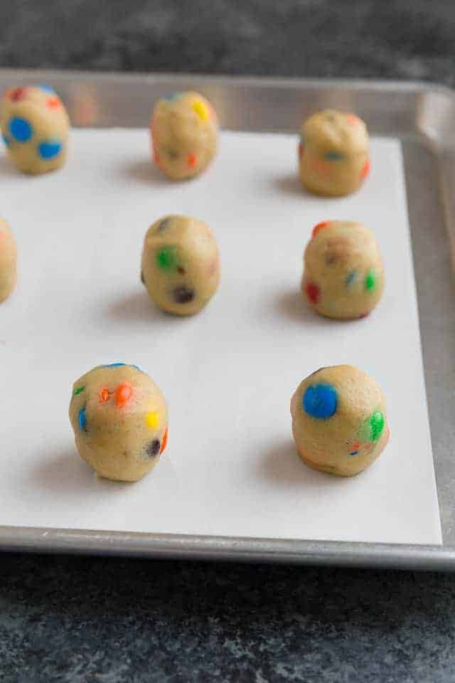 Balls of M&M cookie dough on an aluminum baking sheet lined with parchment paper.