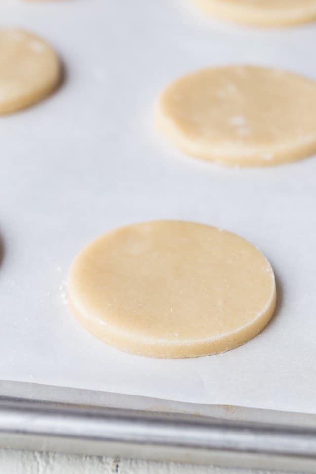 Unbaked soft ice cream sandwich cookies on a baking sheet lined with white parchment paper.