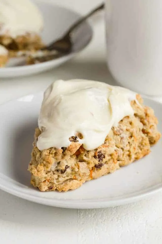 A carrot cake scone topped with cream cheese icing on a white plate.