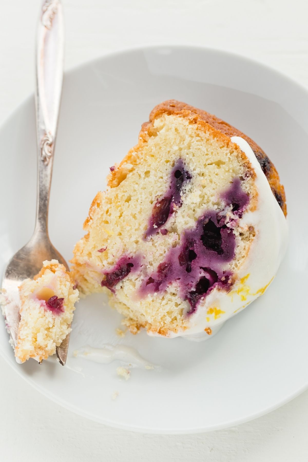 lemon blueberry bundt cake slice on a white plate with a fork taking a bite out