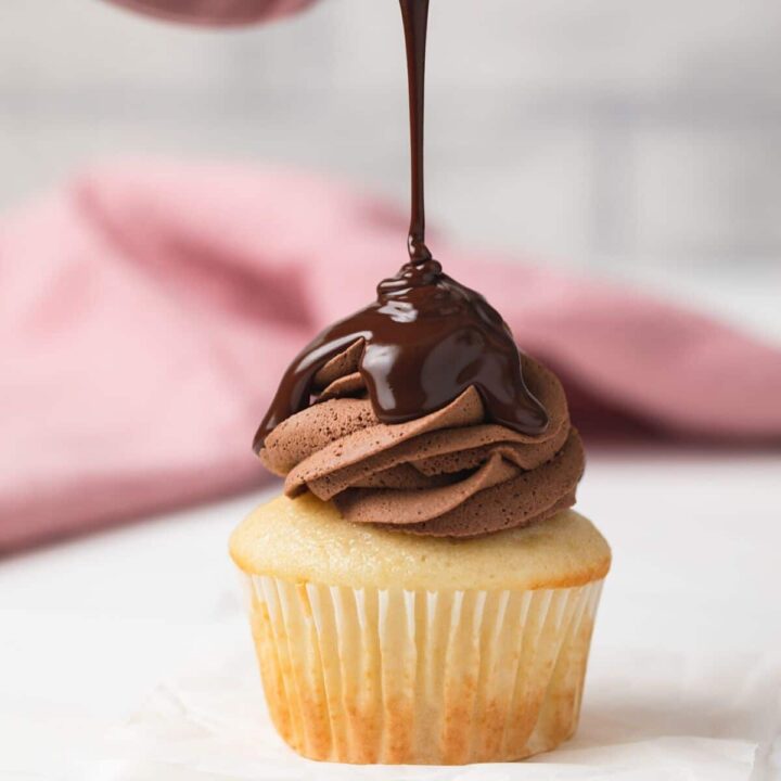 chocolate glaze being poured over chocolate frosting on a vanilla cupcake