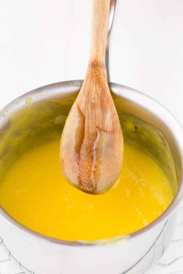 Lemon curd in a stainless steel pot with a wooden spoon.