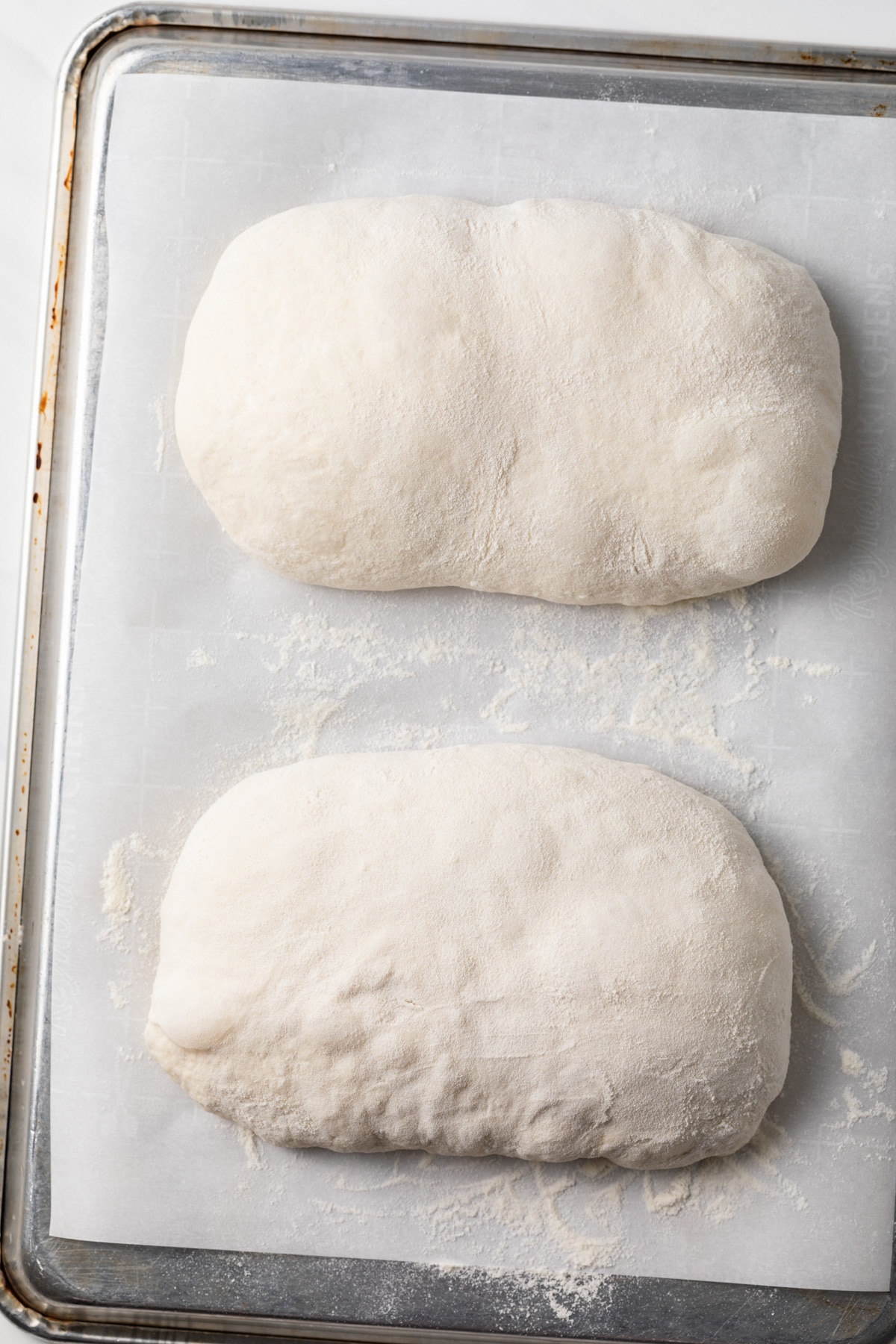 two loaves of unbaked ciabatta on inverted baking sheet lined with parchment paper